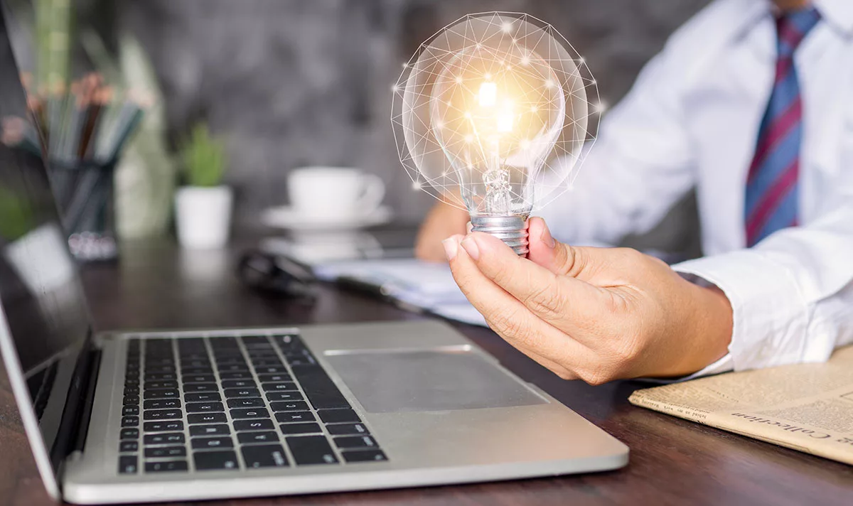 Businessperson holding a glowing light bulb over laptop on desk