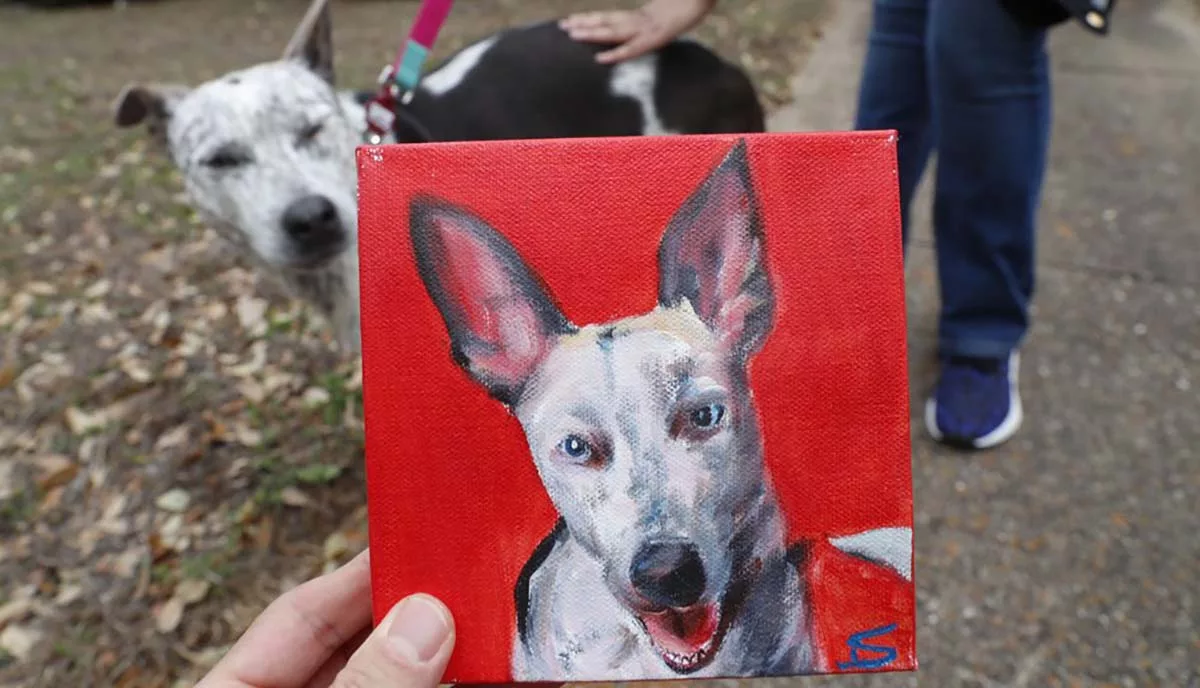 Hand holding dog portrait painting with similar dog in background
