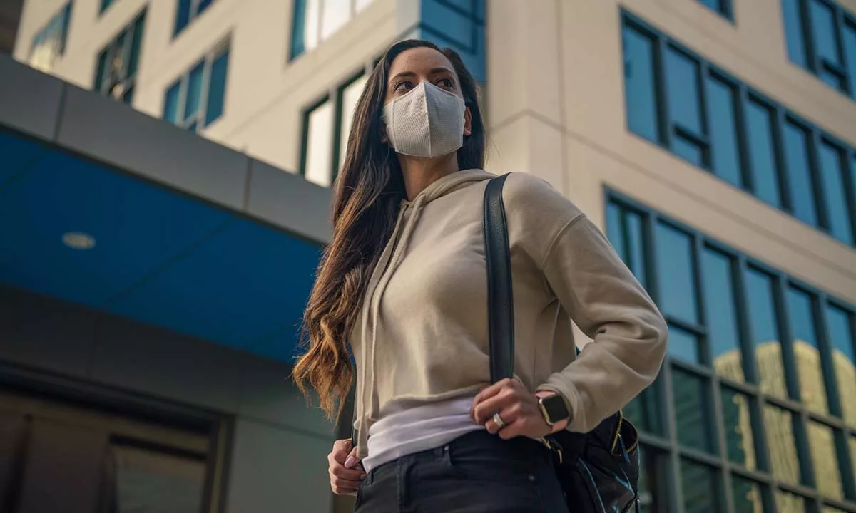 Woman wearing facemask carrying backpack in urban setting