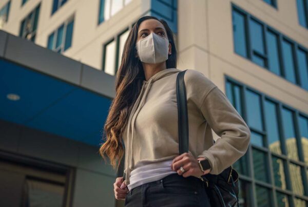 Woman wearing mask walking in city with office buildings in background