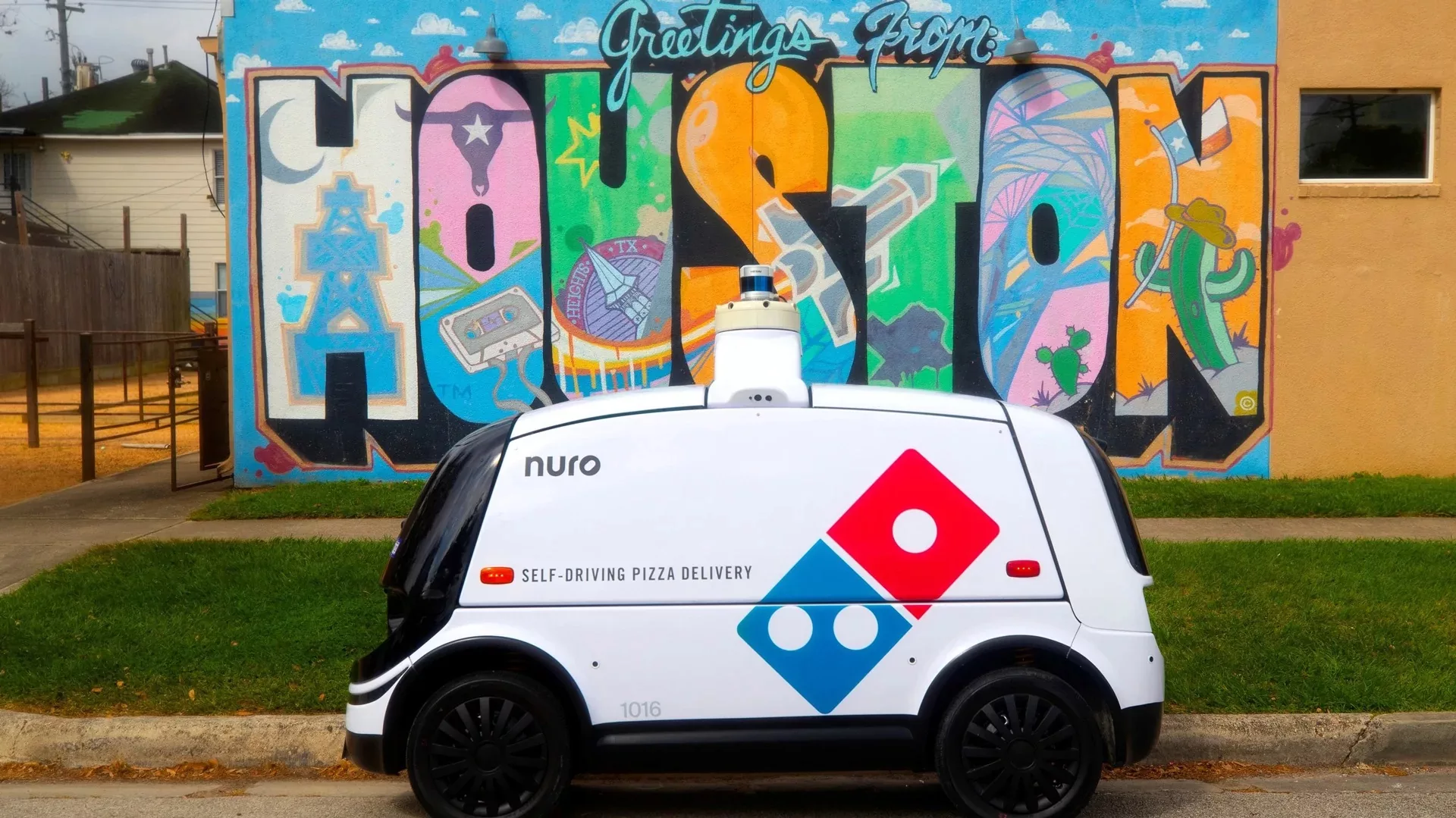 Nuro self-driving pizza delivery vehicle in front of colorful Houston mural.