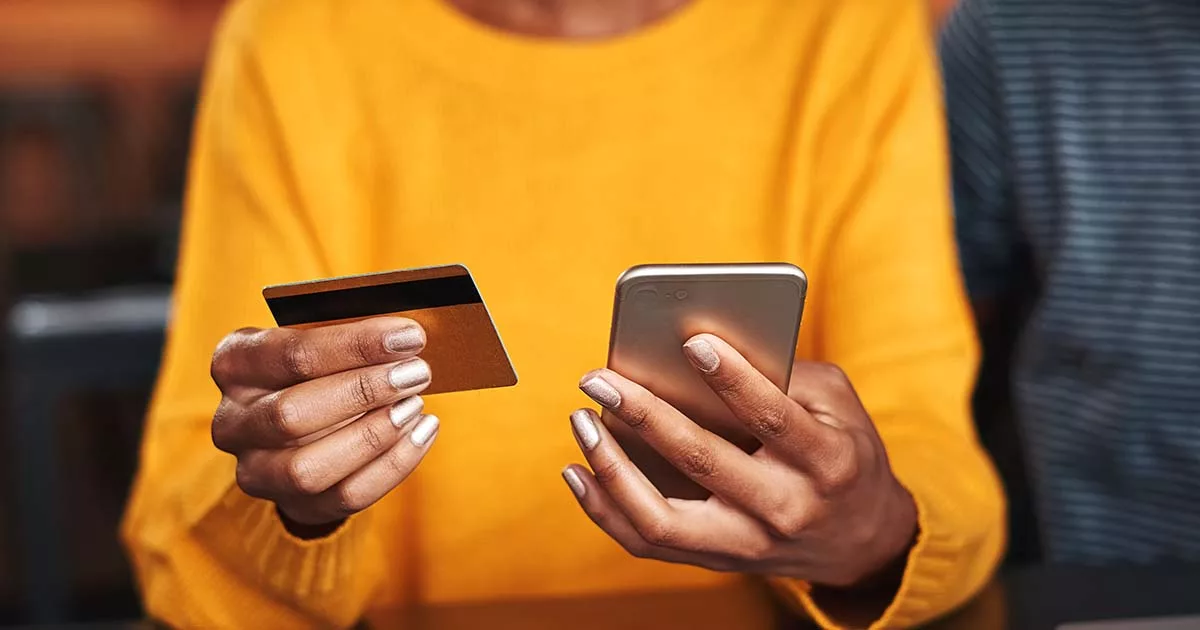 Person in yellow holding credit card and smartphone for online shopping