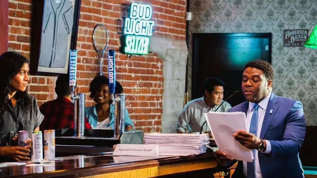 Man in suit reading papers at bar with bartender and neon signs in background