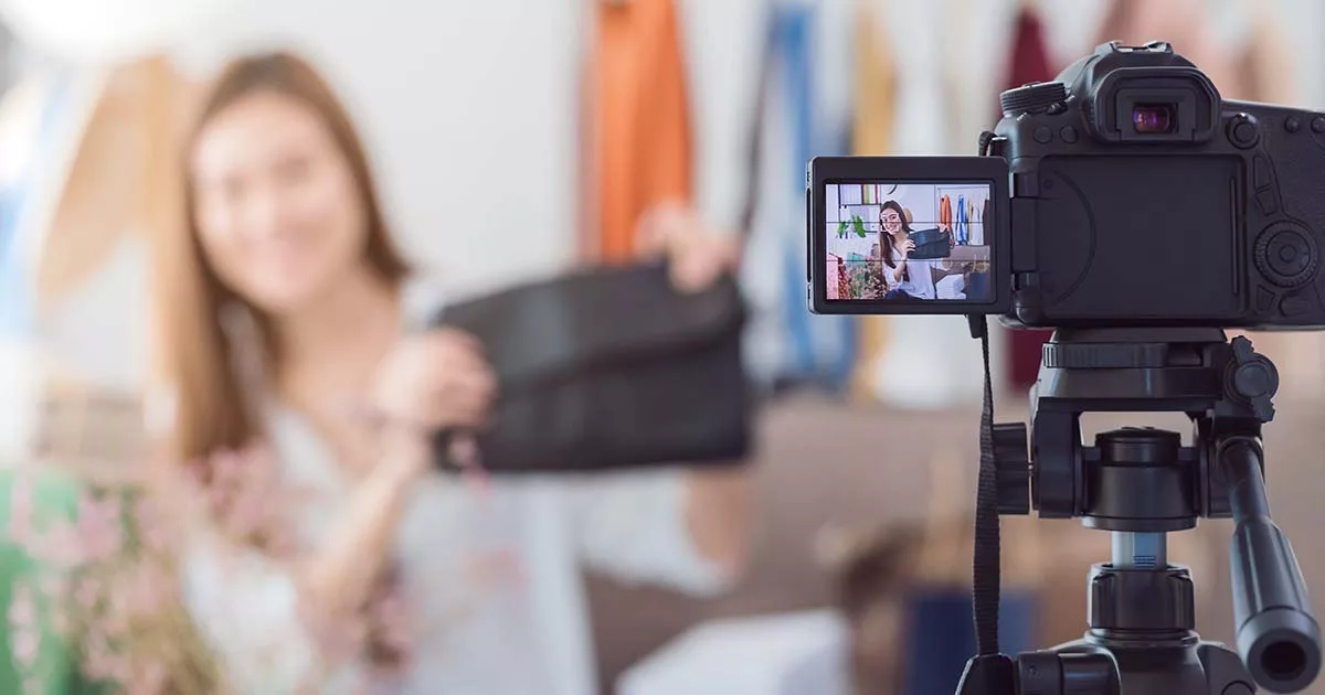 Fashion blogger recording video with DSLR camera on tripod.