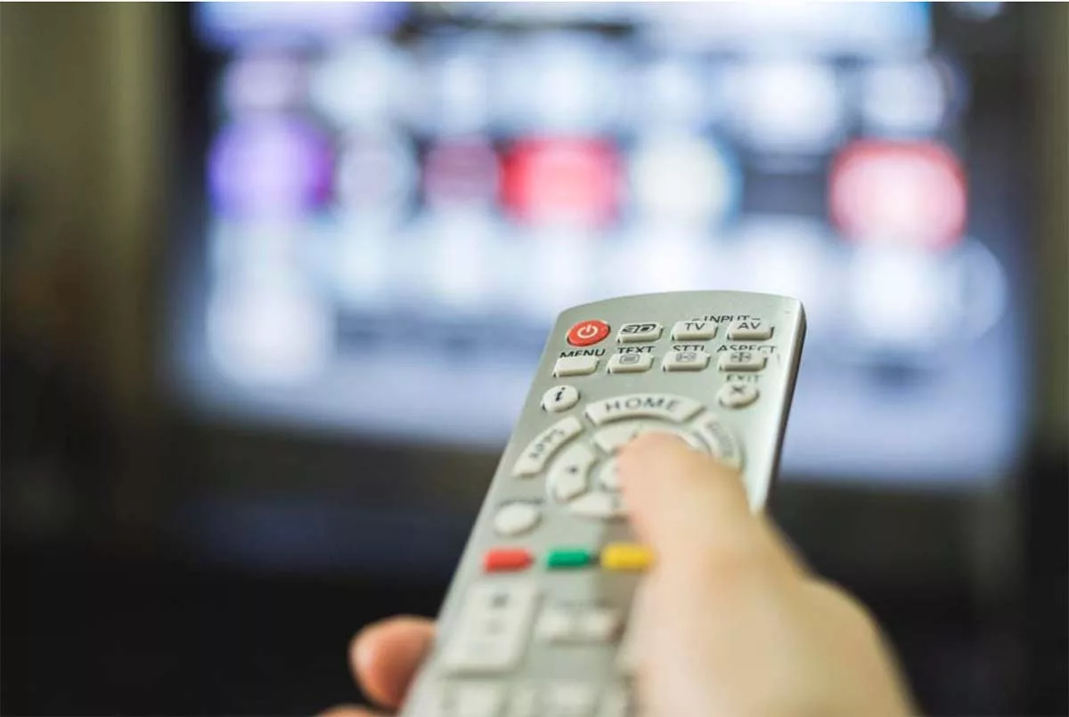 Hand holding a TV remote control with blurred screen in background