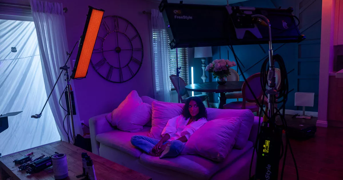 Woman relaxing on sofa in a room with film lighting equipment and purple hue.