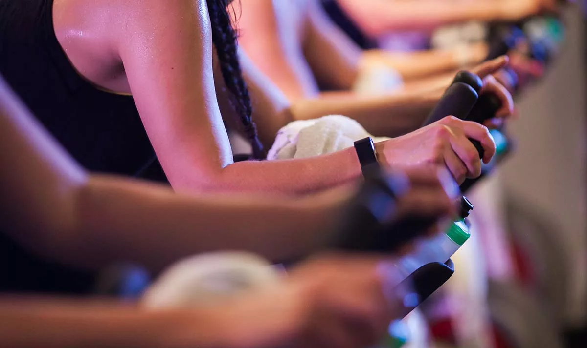 Close-up of an indoor cycling class focusing on participants' arms and handlebars.
