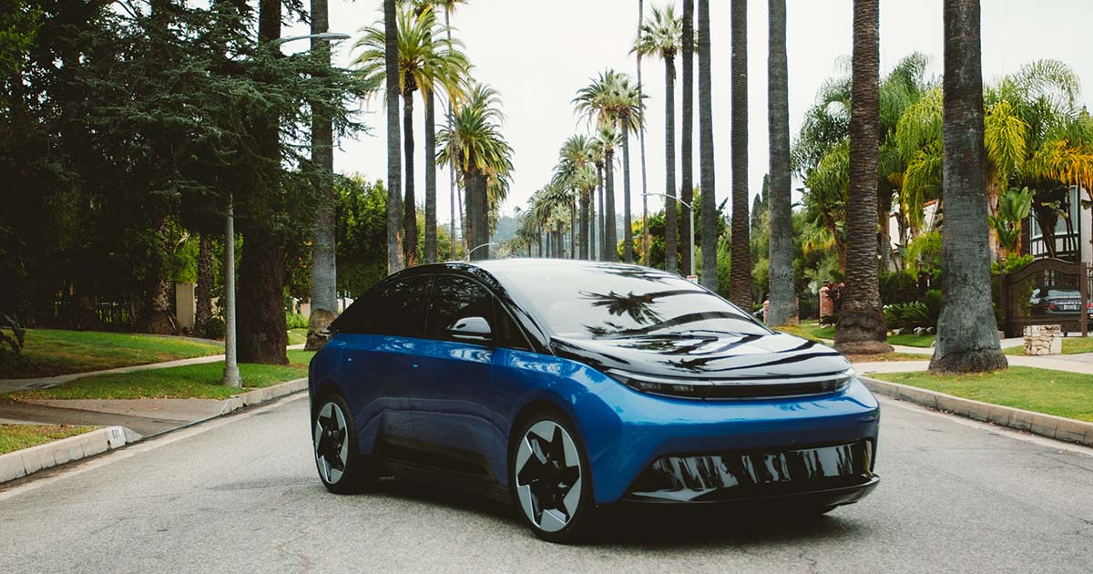 Blue electric car on palm-lined street with reflections on hood