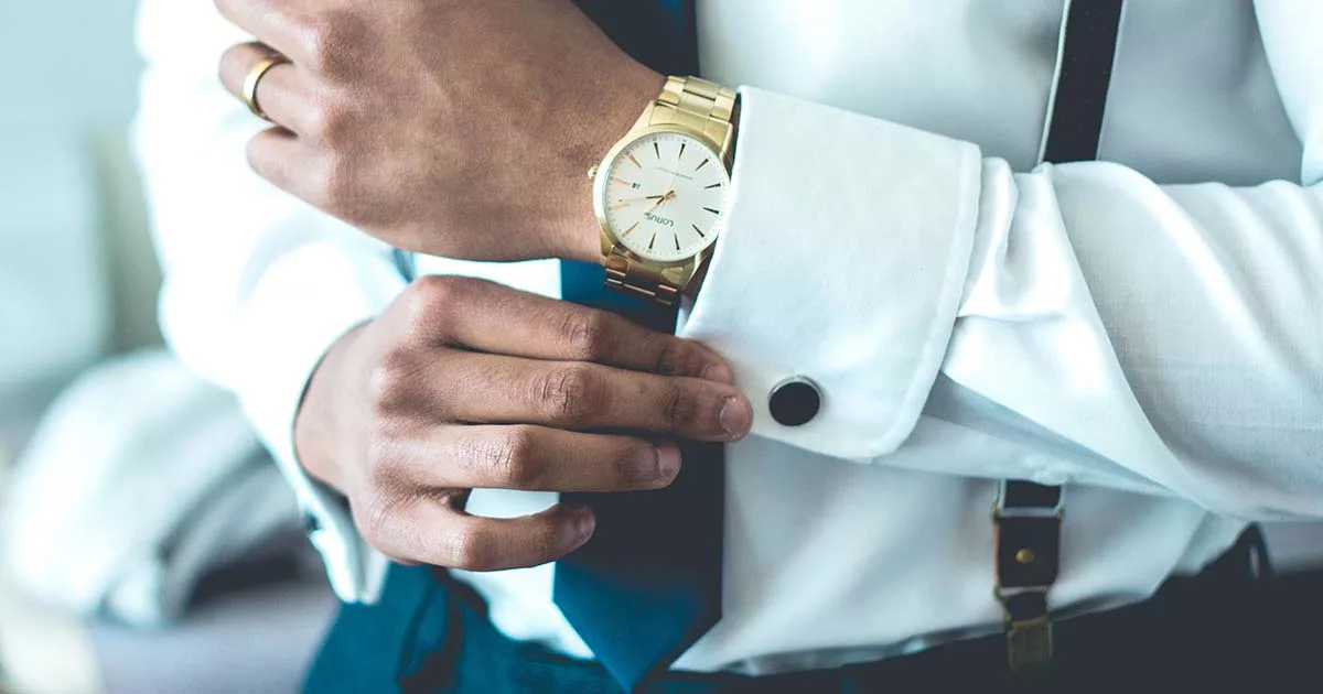 Man adjusting stylish gold wristwatch while wearing white shirt and suspenders