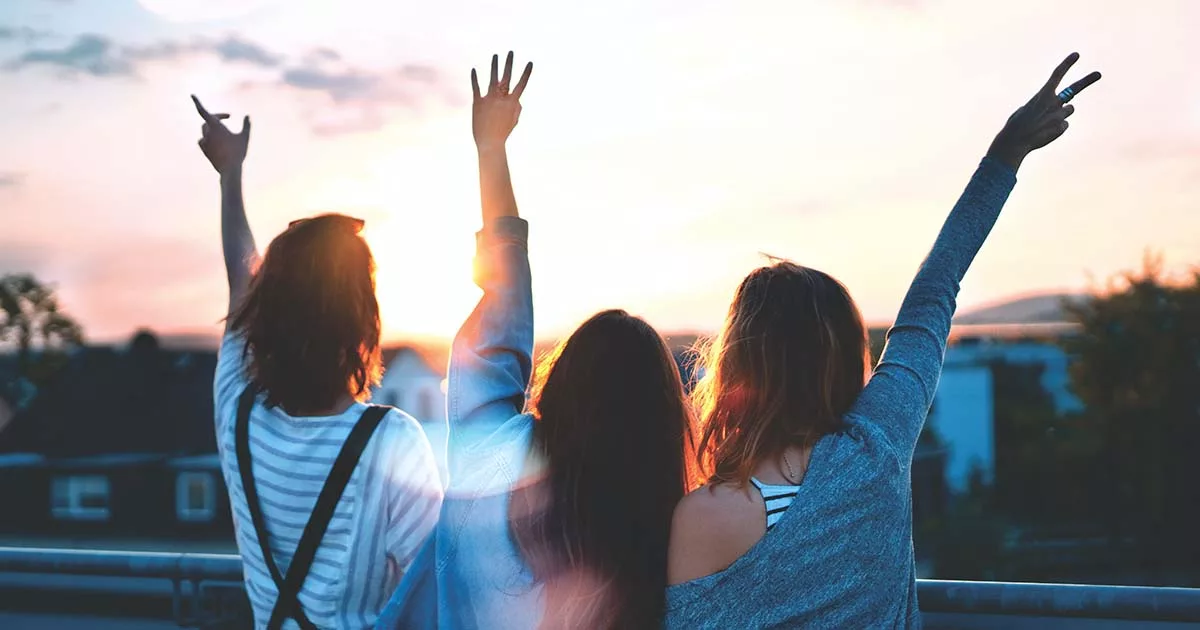 Three friends with raised hands enjoying sunset together.