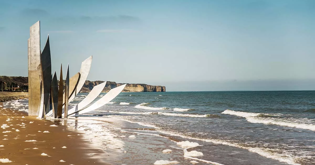 Abstract metal sculpture on a sandy beach with waves and cliffs in the background