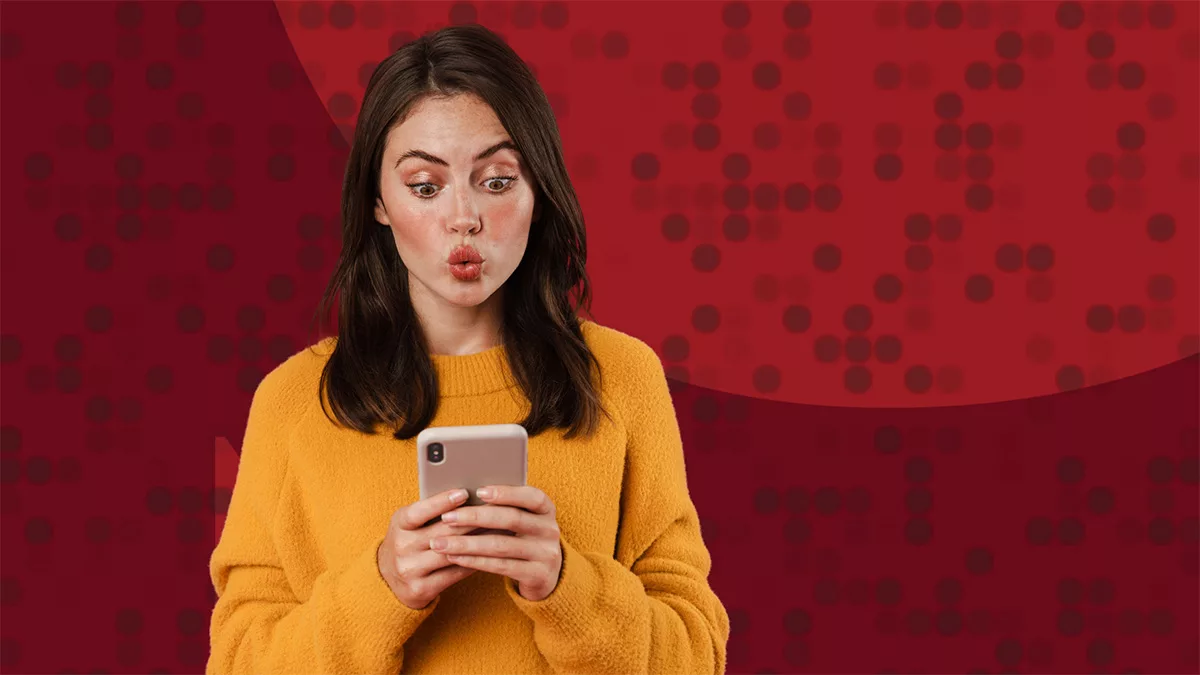 Surprised woman in yellow sweater looking at smartphone with red dotted background