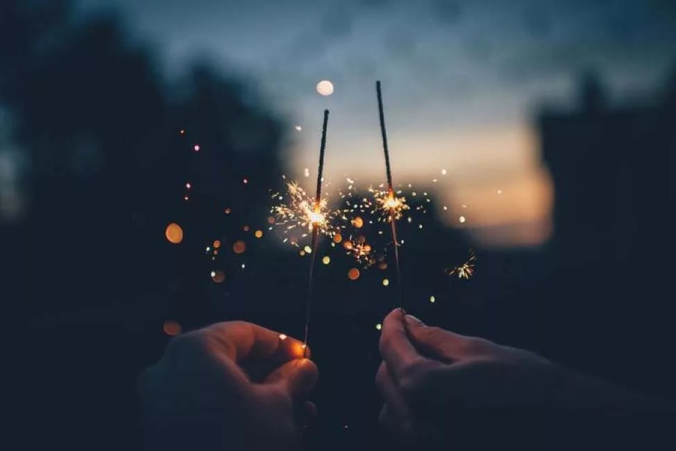 Hands holding sparklers with glowing sparks at twilight