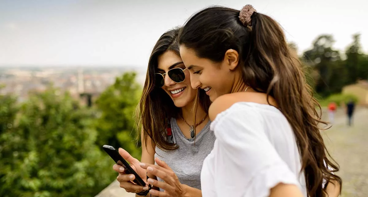 Two joyful women looking at smartphone with cityscape in background