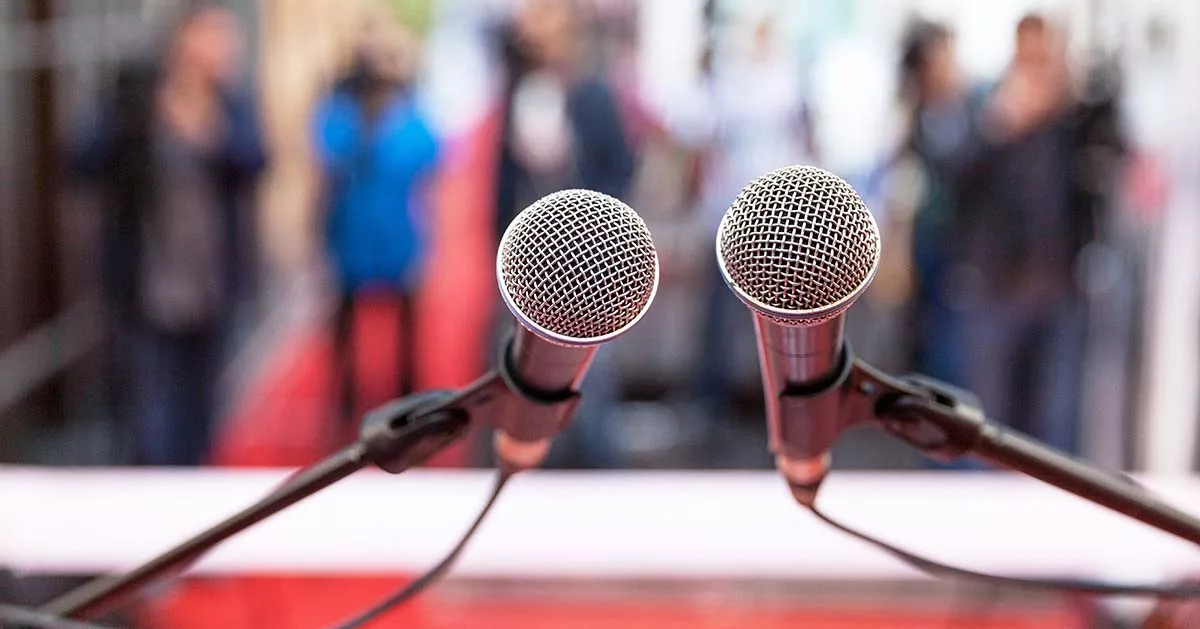 Two microphones on stand with blurred audience in background