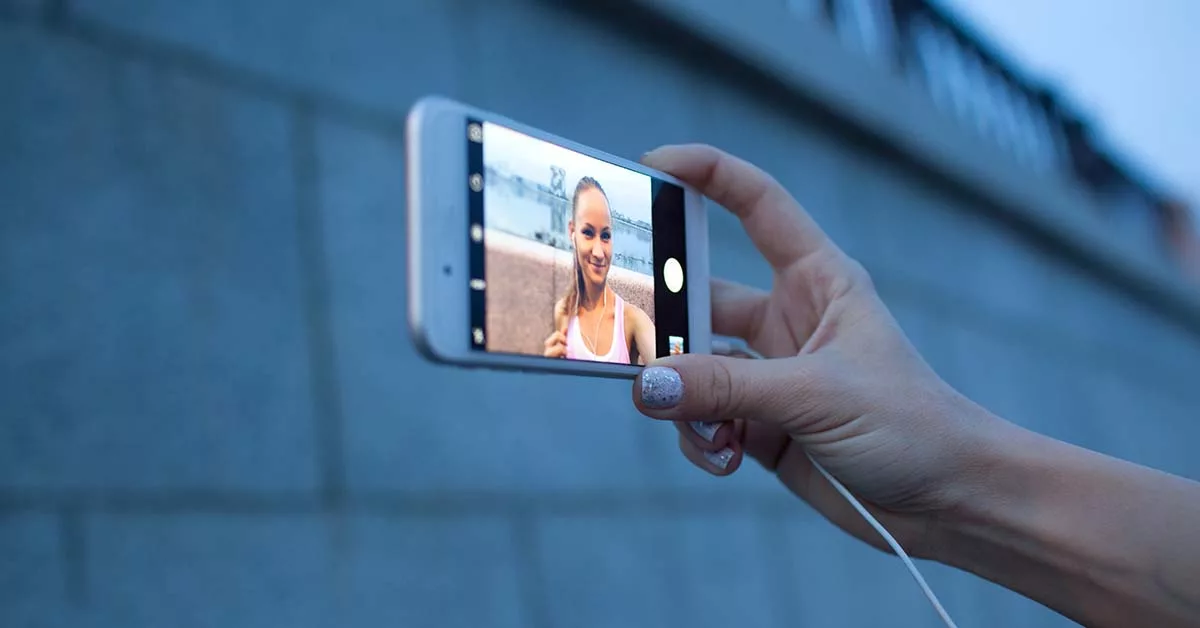 Hand holding smartphone taking selfie of smiling woman outdoors