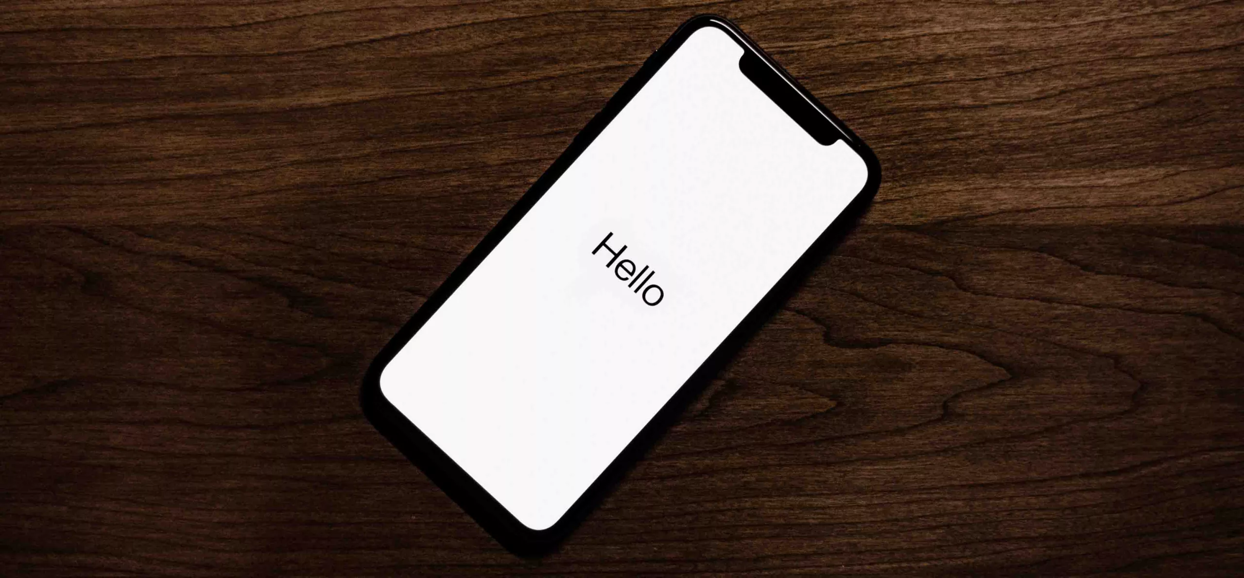 Smartphone with 'Hello' on screen placed on a wooden table.