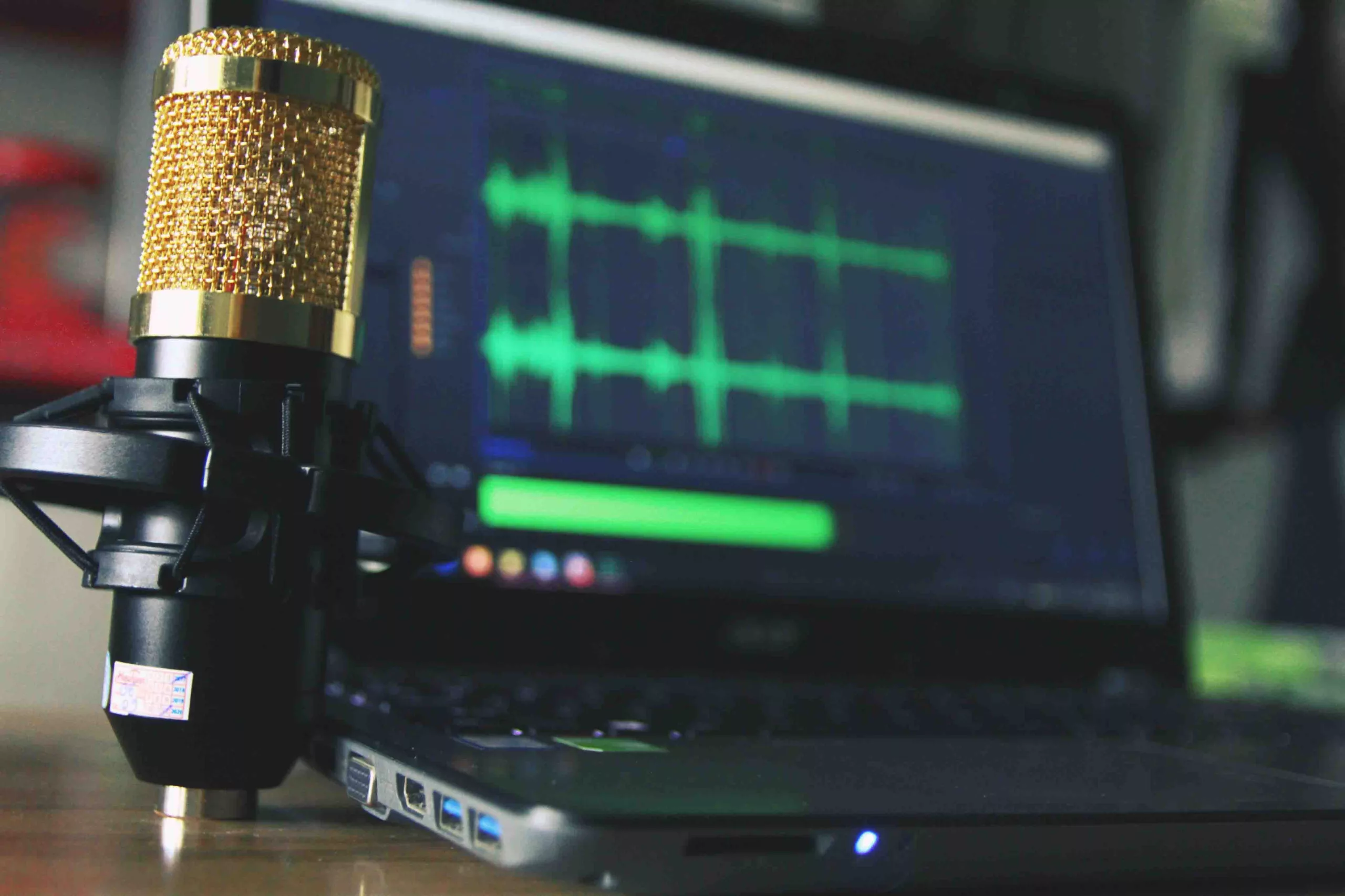 Gold microphone in focus with waveform on laptop screen in the background