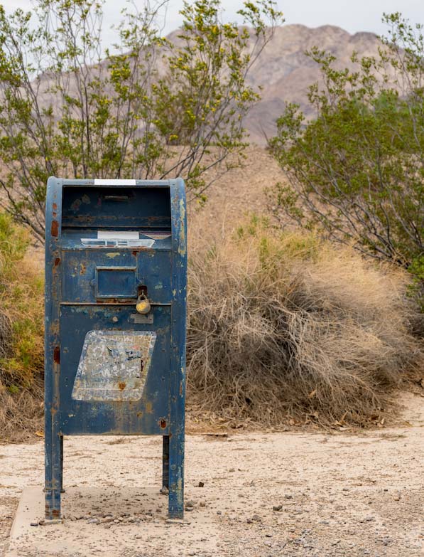 Weathered blue mailbox in desert landscape with mountains in background