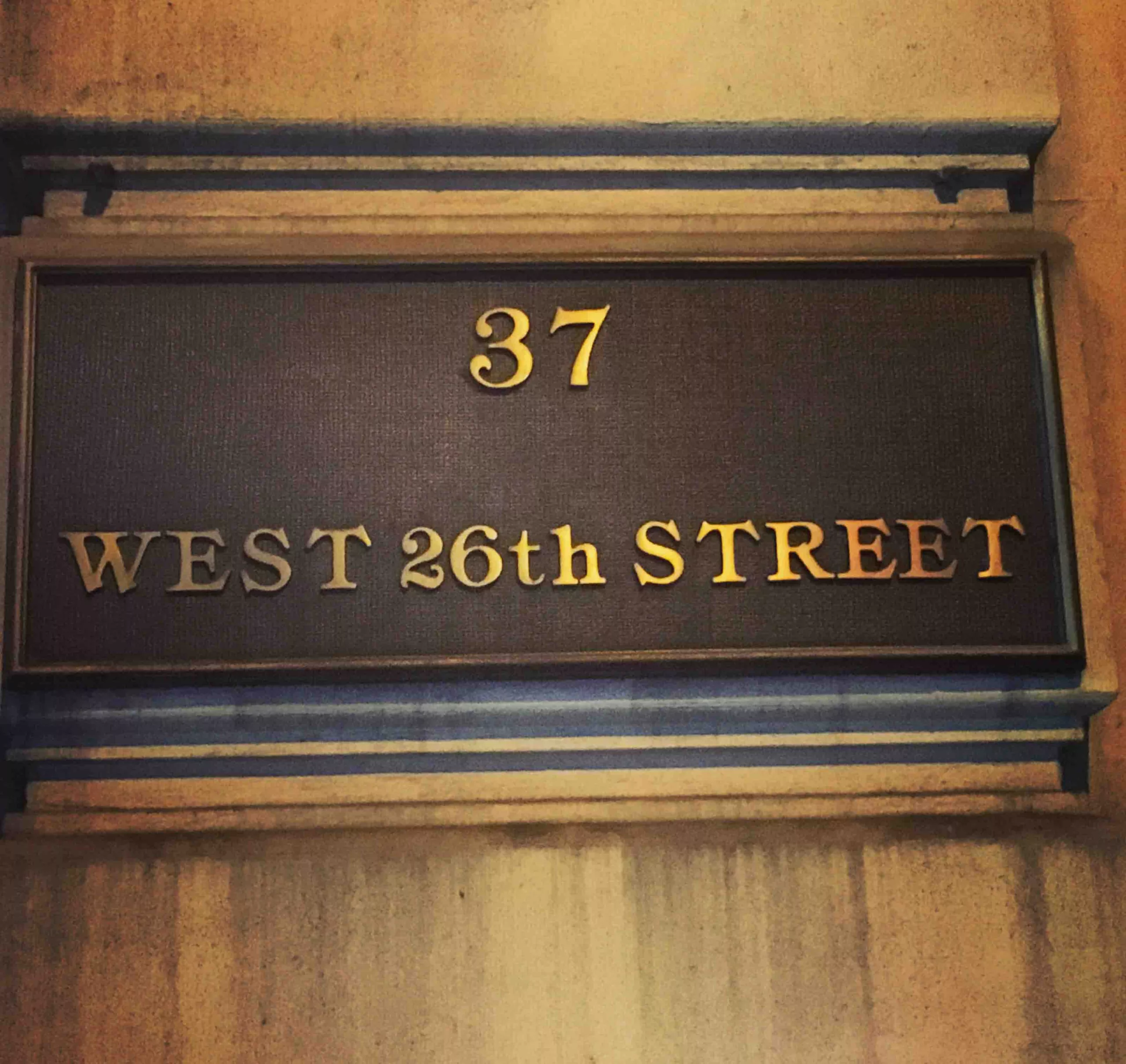 Elegant gold-lettered sign reading '37 WEST 26th STREET' mounted on a building facade.