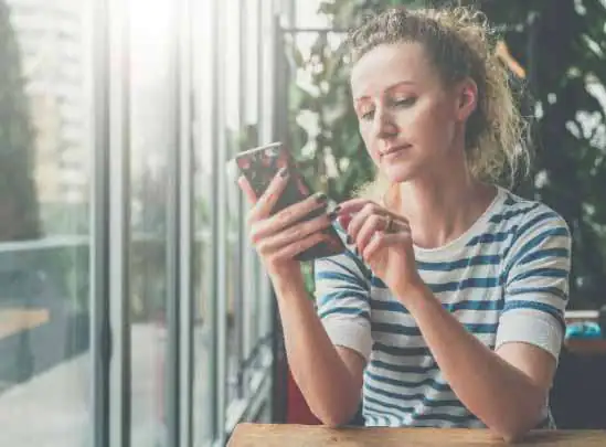 Woman in striped shirt using smartphone by large windows