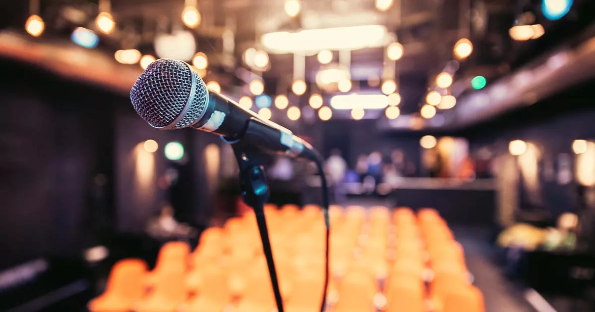 Microphone on stage with blurred orange audience seating and bokeh lights
