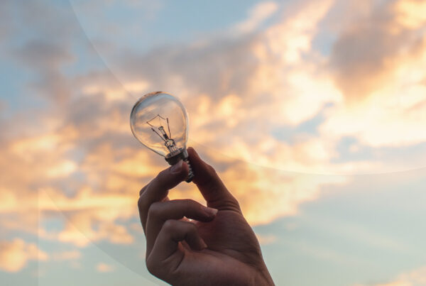 Hand holding light bulb against a vibrant cloudy sunset sky