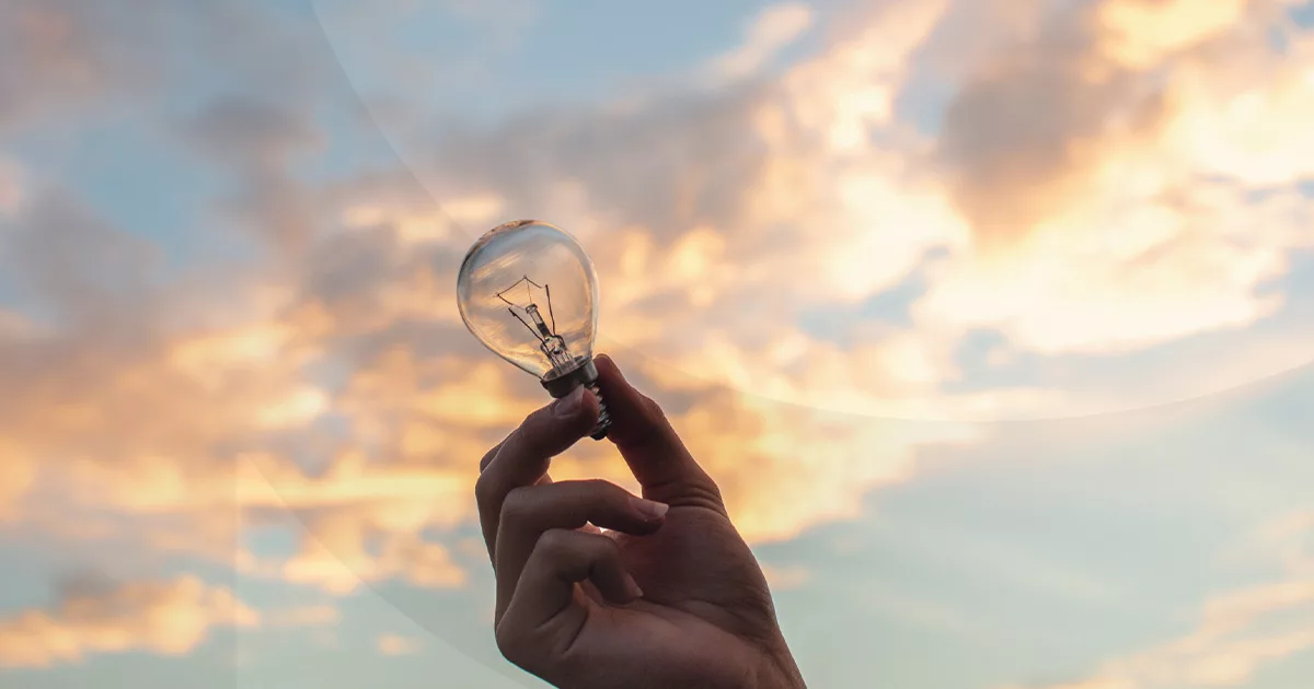 Hand holding light bulb against sunset sky with clouds