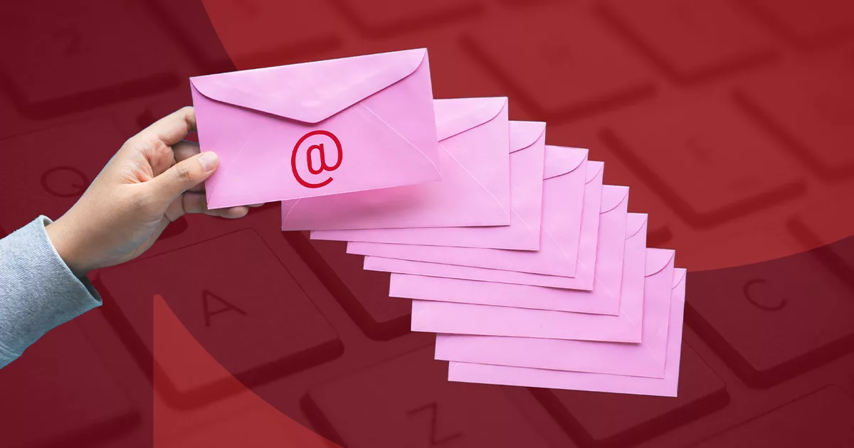 Hand holding a pink email envelope over a pile on a keyboard background.