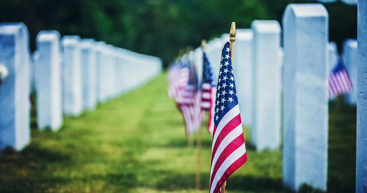 American flag in focus at a cemetery with white headstones in the background