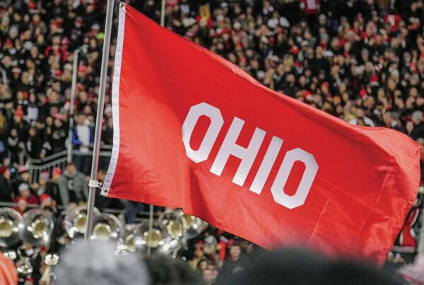 Red Ohio flag waving at crowded sports event with brass instruments visible