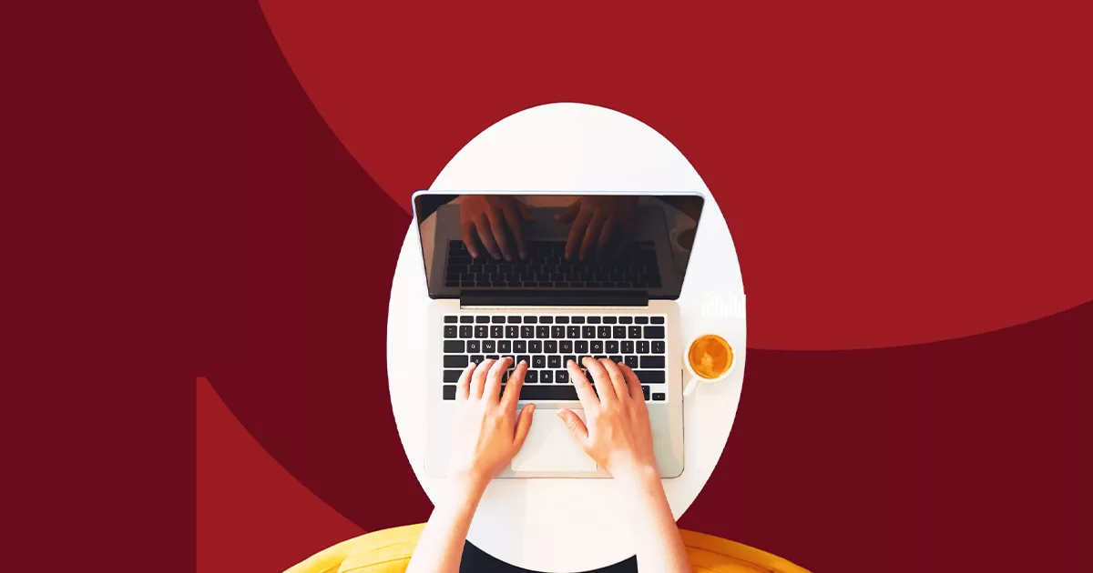 Top view of person working on laptop with coffee on white desk and red background