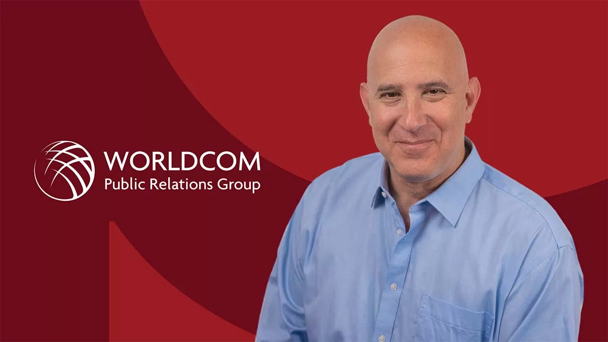 Bald man in blue shirt smiling with Worldcom Public Relations Group logo