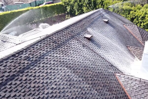 Aerial view of a wet shingle roof being sprayed with water