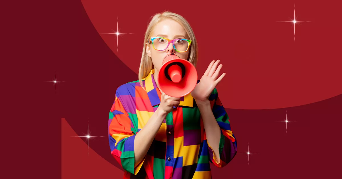 Woman with colorful shirt and glasses speaking into red megaphone against maroon background