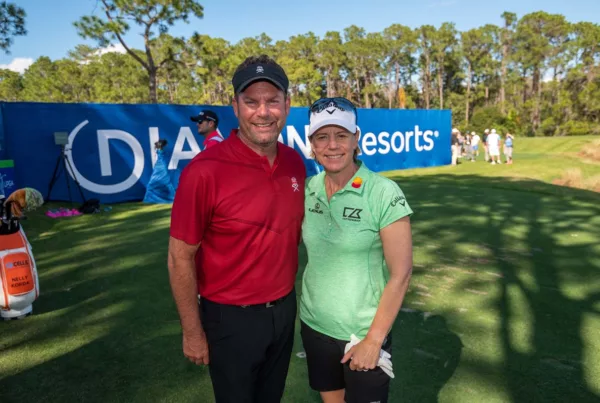 Two golfers smiling at a golf event with sponsor banners in the background.