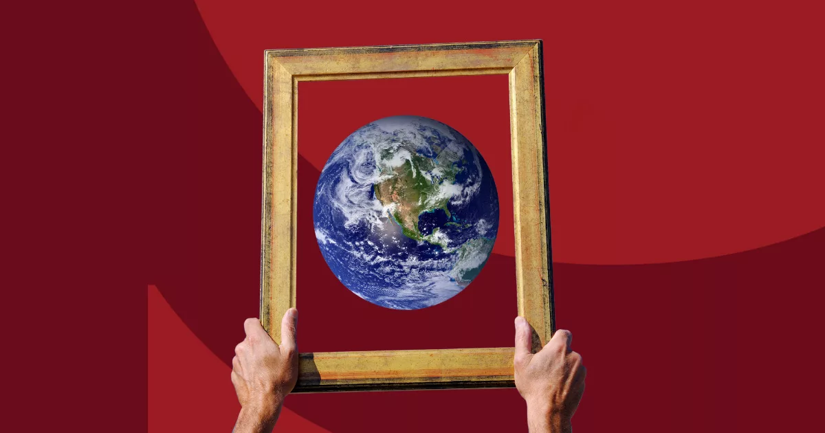 Hands holding a vintage frame with Earth floating inside against a red background