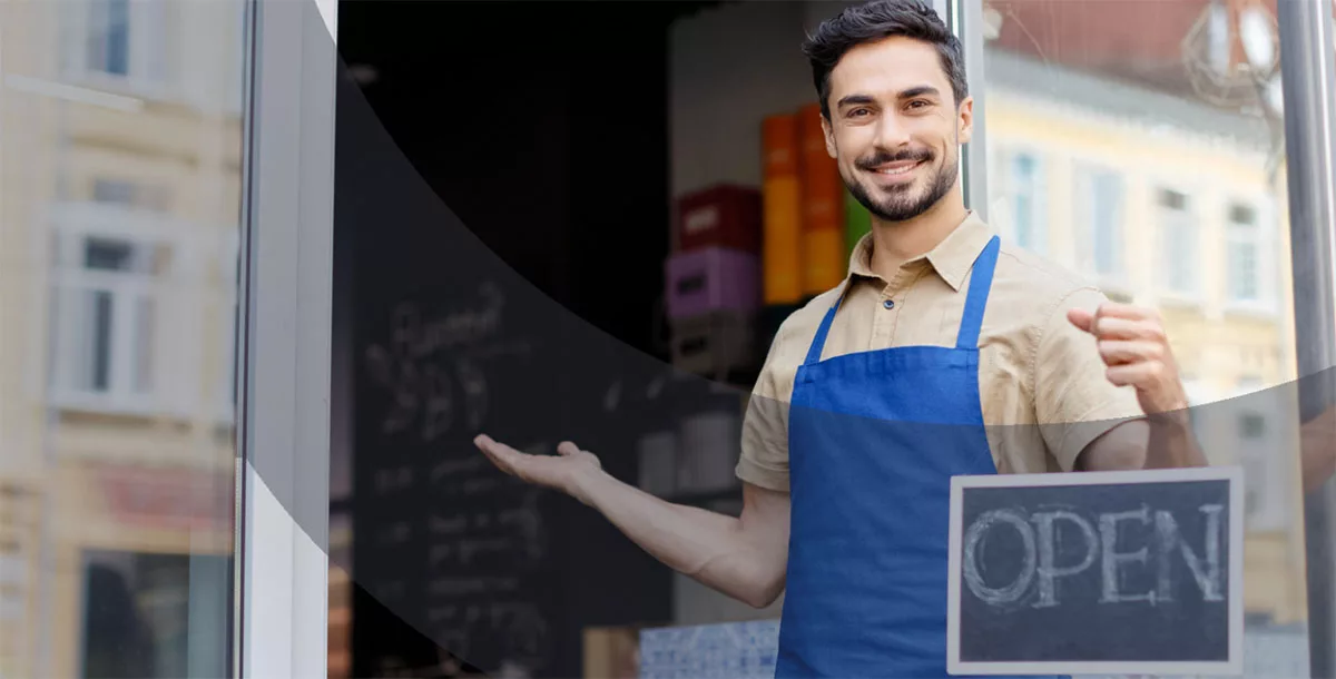 Smiling man with apron holding open sign at cafe entrance