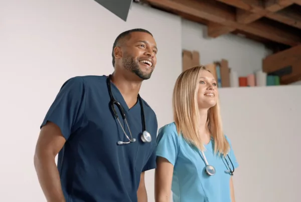 Two smiling healthcare professionals in scrubs with stethoscopes looking upward.