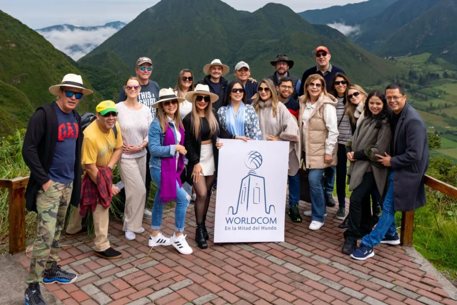 Group of people posing with "Worldcom" sign in front of lush green mountains