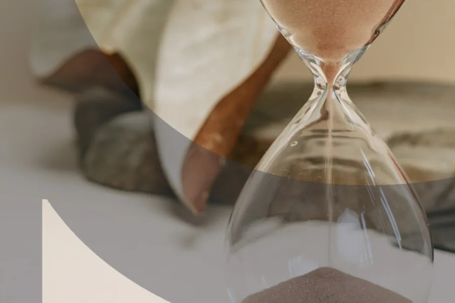 Sand flowing through a glass hourglass on a textured stone surface
