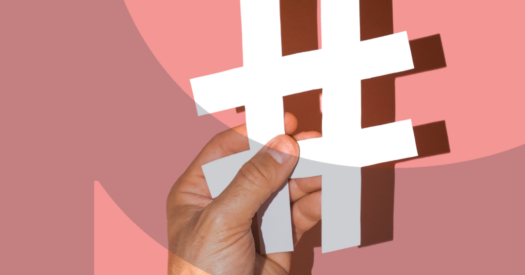 Hand holding a large white hashtag cutout against a pink background