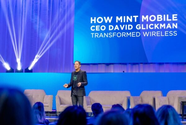 David Glickman speaks on stage about transforming wireless with Mint Mobile at a tech conference, with vibrant lighting.