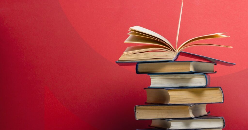 A stack of books with one open book on top of them against a red background.