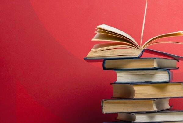 A stack of books with one open book on top of them against a red background.