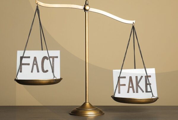 Scales balancing two notecards that say "fact" and "fake" respectively