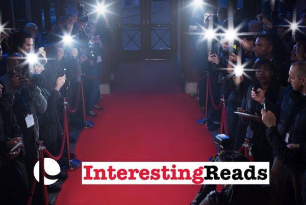 A red carpet leading to the door with paparazzi and cameras flashing behind ropes to the left and right of the carpet.