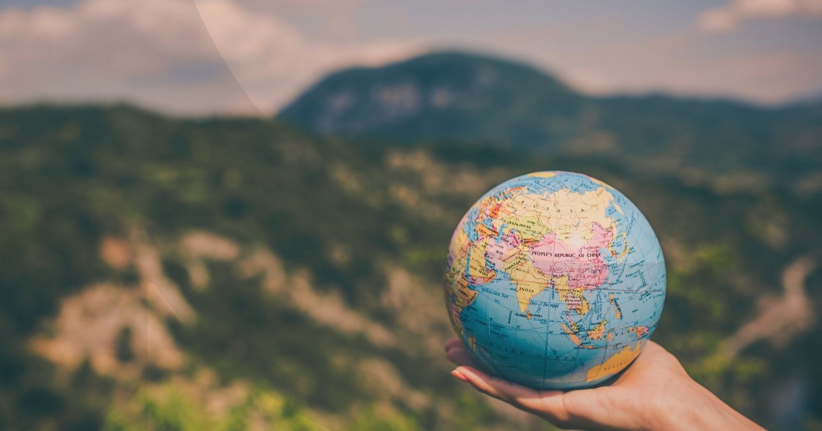 Hand holding a small version of a globe in the middle of a forest
