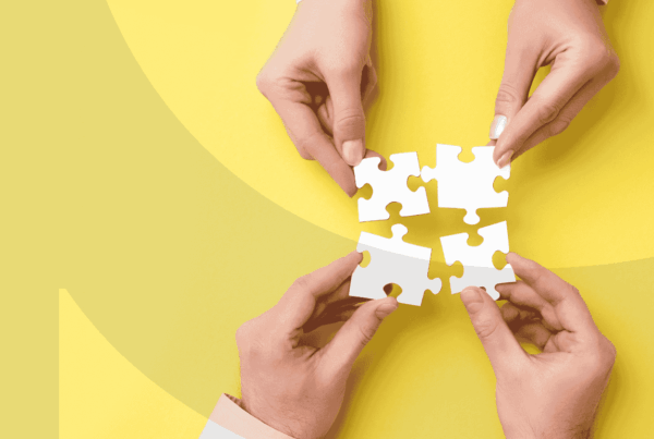 Four hands putting together four puzzle pieces on a yellow background