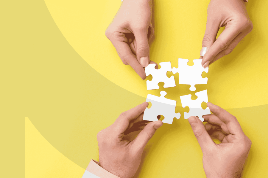 Four hands putting together four puzzle pieces on a yellow background